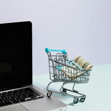 Mini shopping cart with rolled cash next to a laptop, representing online shopping.